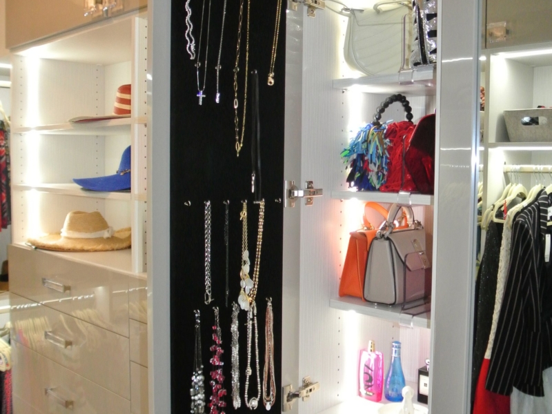 Custom closet with white cabinetry, lighted shelves, and a jewelry cabinet