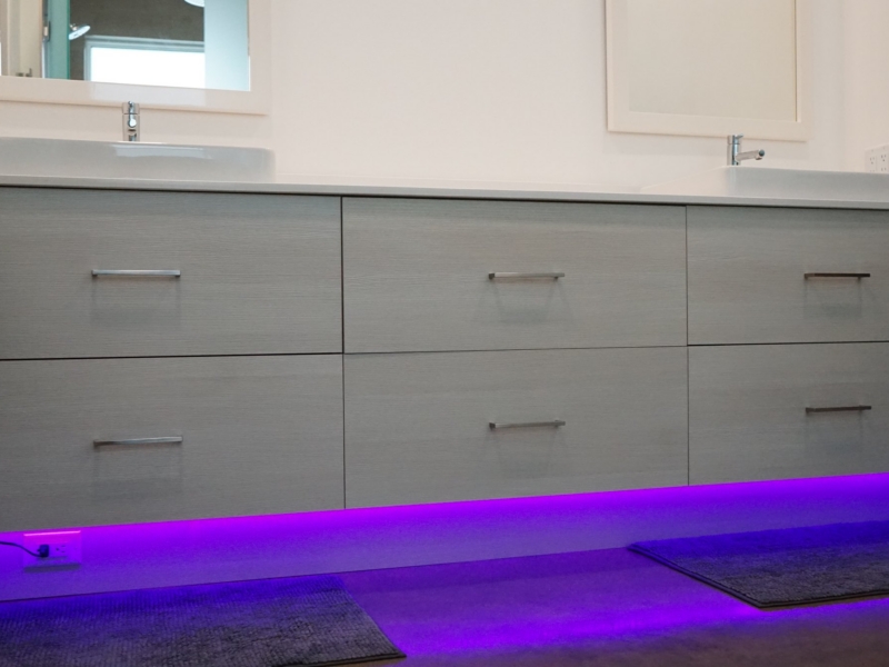 Contemporary gray wood-grain double vanity with LED toe-kick lighting