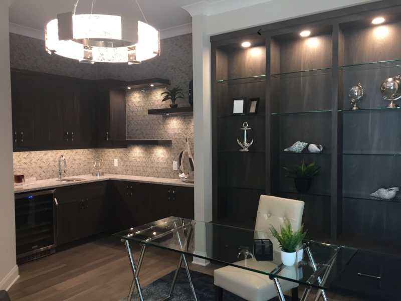 Dark wood bar cabinetry and lighted glass display shelving beside a home office