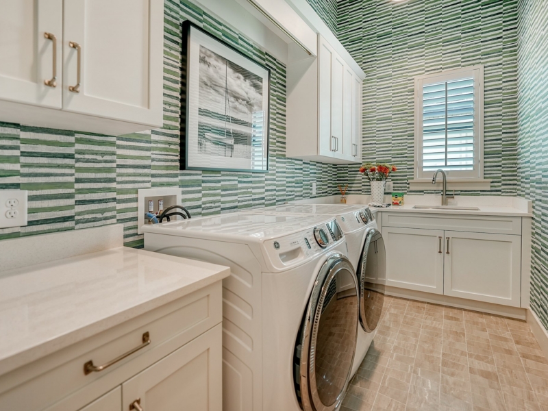 Laundry room with white custom cabinets and green striped tile