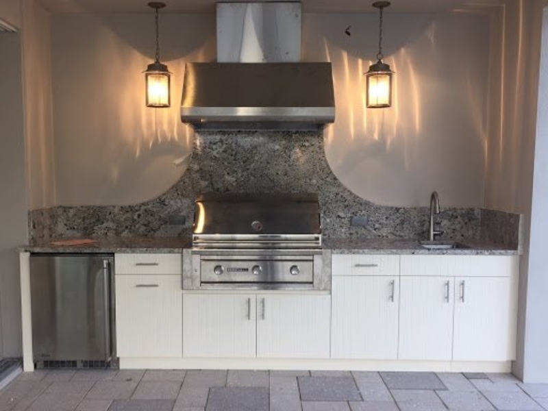 Outdoor kitchen with white custom cabinets, a built-in grill, and a granite backsplash