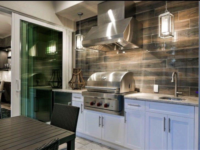 Outdoor kitchen with white custom cabinets, a built-in grill, and a stainless hood